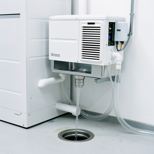 Installation technique montrant une unité de climatisation avec bac de récupération, tuyau d’évacuation des condensats, siphon et pompe de relevage dirigeant l’eau vers une évacuation au sol.
