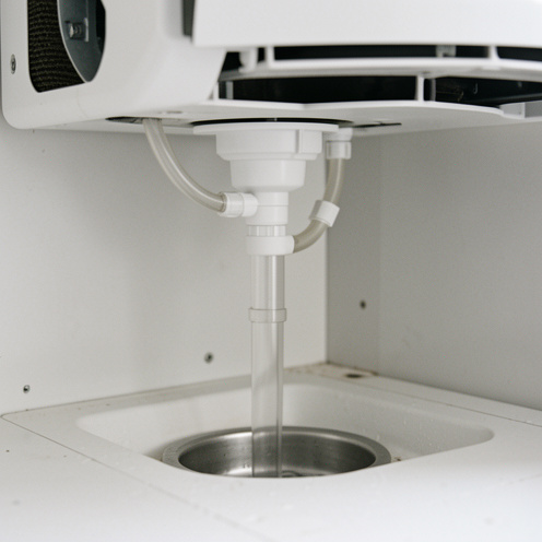 Siphon vertical raccordé à l’évacuation des condensats d’un système de climatisation, avec tuyaux transparents et bac de récupération.